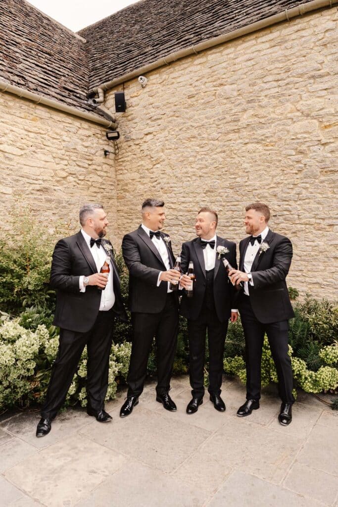 groom and groomsmen toast beer bottles in gardens of caswell house